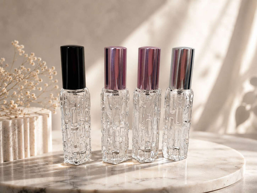 Four crystal perfume bottles with different colored caps on a marble surface.